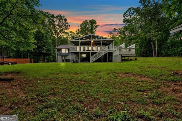 back of house at dusk featuring stairway, a deck, and a yard