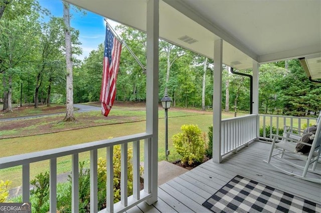 deck featuring a porch, view of wooded area, and a yard