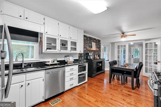 kitchen with stainless steel appliances, dark countertops, a ceiling fan, light wood-type flooring, and white cabinetry