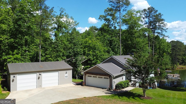 view of front of home with a detached garage, a front lawn, metal roof, an outdoor structure, and a water view