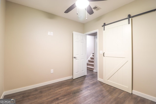 unfurnished bedroom with a barn door, dark wood finished floors, baseboards, and ceiling fan