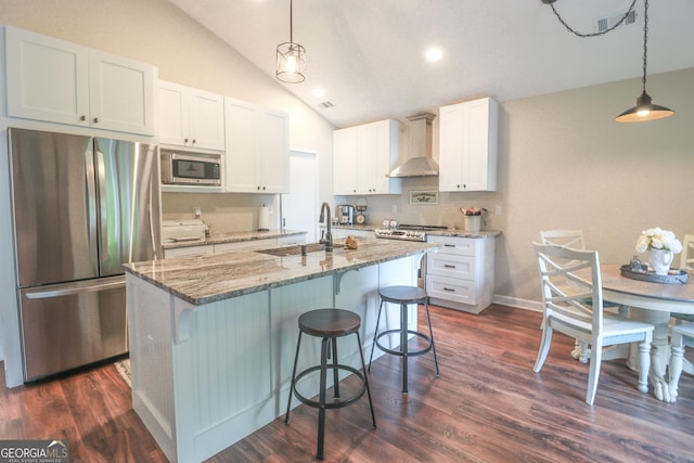 kitchen featuring appliances with stainless steel finishes, a sink, wall chimney exhaust hood, lofted ceiling, and light stone counters