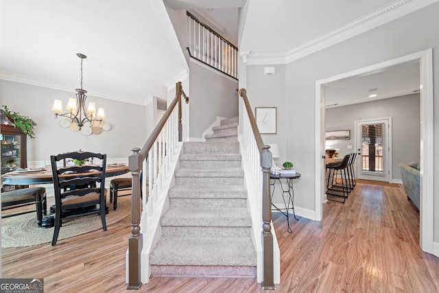 staircase featuring wood finished floors, ornamental molding, baseboards, and a chandelier