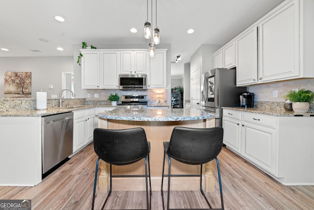 kitchen with stainless steel appliances, a sink, a kitchen island, white cabinets, and recessed lighting