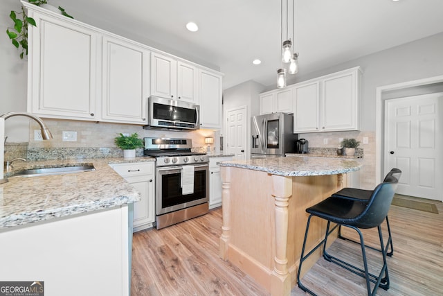 kitchen featuring stainless steel appliances, a sink, light wood-style flooring, a center island, and tasteful backsplash