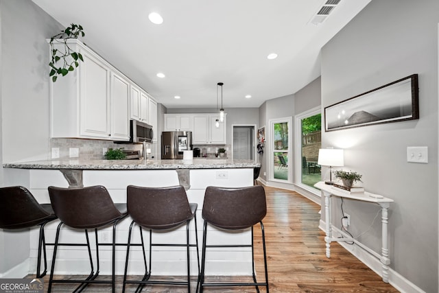 kitchen with appliances with stainless steel finishes, a peninsula, light wood finished floors, white cabinets, and recessed lighting