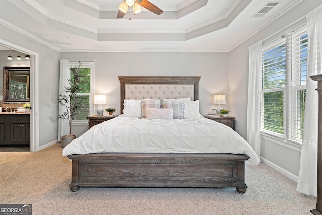 bedroom featuring light carpet, ensuite bathroom, a raised ceiling, ornamental molding, and baseboards