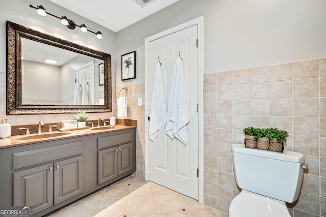 bathroom with tile walls, tile patterned flooring, toilet, double vanity, and a wainscoted wall