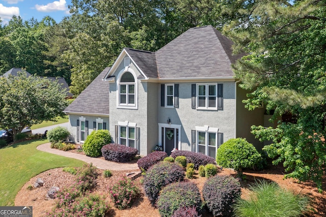 colonial home with stucco siding, a front lawn, and a shingled roof