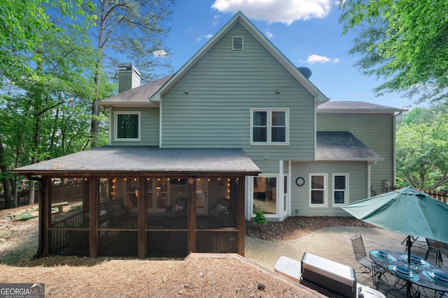 rear view of property with a sunroom, a patio, roof with shingles, and a chimney