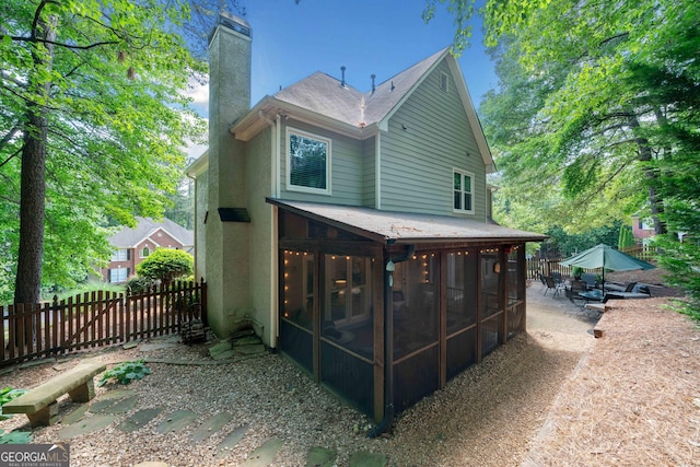 rear view of house with a sunroom, a chimney, fence, a shingled roof, and a patio