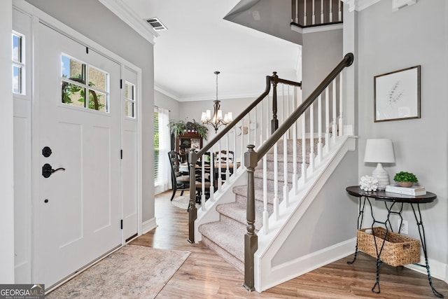 entryway featuring wood finished floors, ornamental molding, stairs, a chandelier, and baseboards