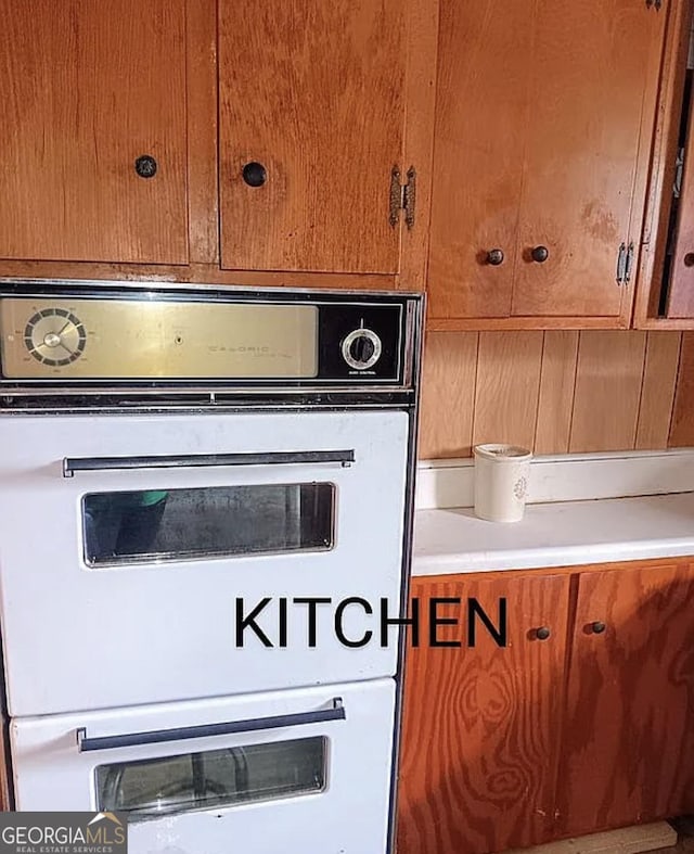 kitchen view of brown cabinets, double oven, and light countertops