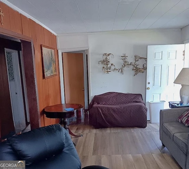 living area featuring light wood-style floors, wooden walls, and ornamental molding