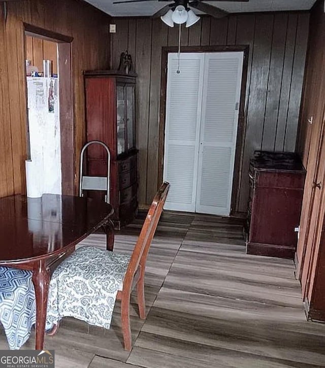 dining space with wood walls, a ceiling fan, and wood finished floors