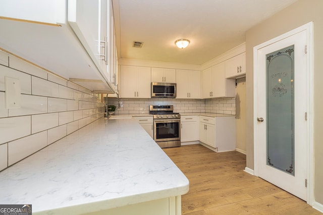 10 Queens Ct, Sharpsburg, GA 30277 - kitchen with appliances with stainless steel finishes, decorative backsplash, white cabinetry, and light wood finished floors