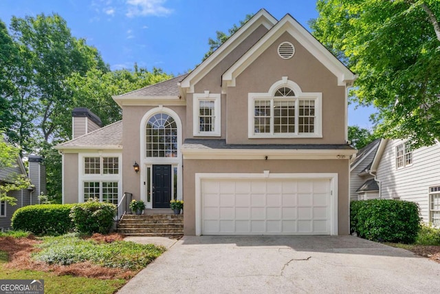 traditional-style home featuring stucco siding, a garage, driveway, and a chimney