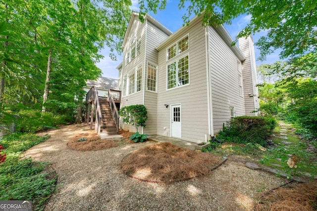 back of house with stairs, a chimney, and a deck