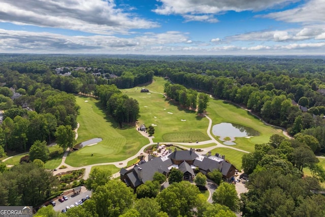 view of property location featuring a golf course, a heavily wooded area, and a nearby body of water