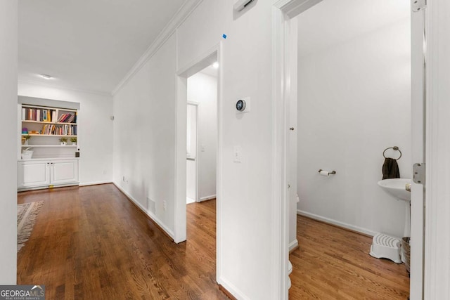 hall featuring ornamental molding, wood finished floors, baseboards, and built in shelves