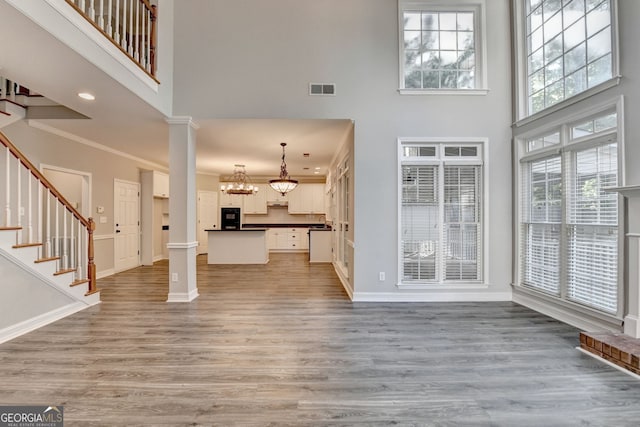 2049 Mclain Rd NW, Acworth, GA 30101 - unfurnished living room with ornate columns, a towering ceiling, baseboards, light wood-type flooring, and stairway