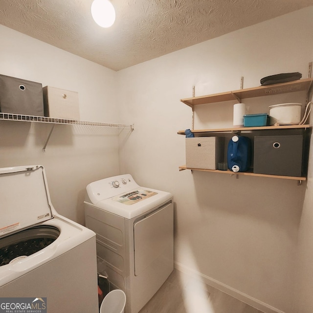 laundry area featuring washing machine and clothes dryer, baseboards, and a textured ceiling