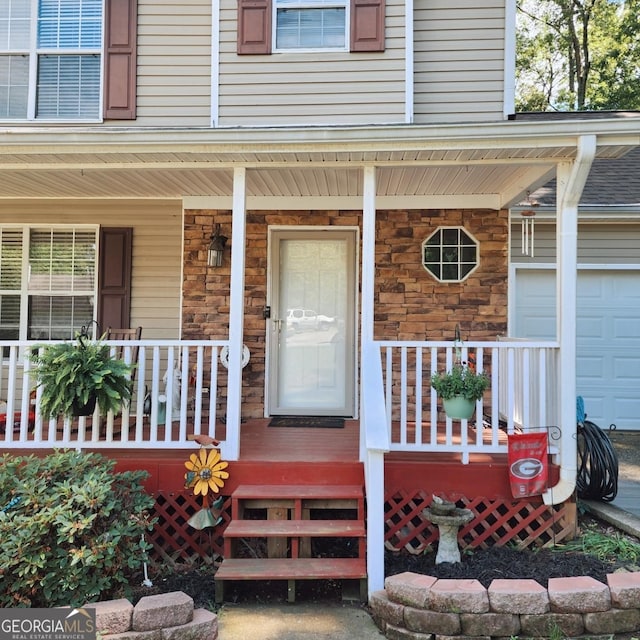 entrance to property with covered porch, stone siding, and a garage