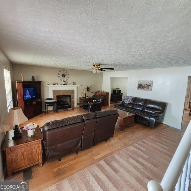 living area featuring light wood-style floors, a textured ceiling, ceiling fan, and a tiled fireplace