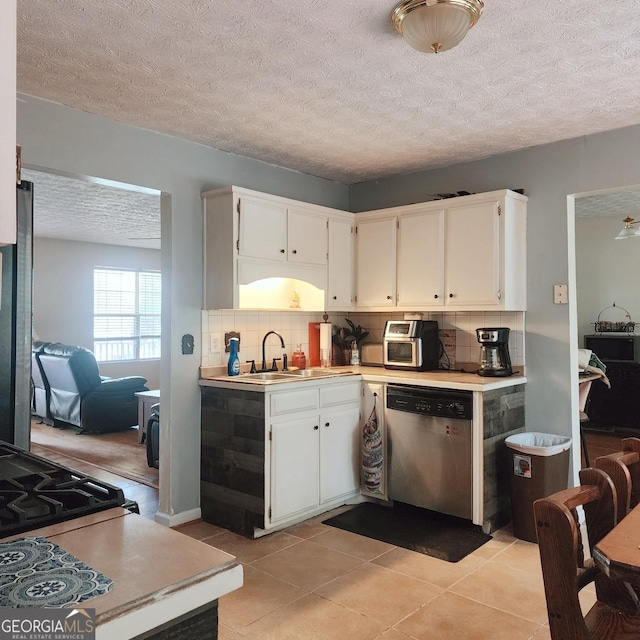 kitchen with stainless steel dishwasher, a sink, tasteful backsplash, light countertops, and a textured ceiling