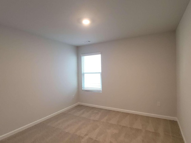 spare room featuring light colored carpet and baseboards