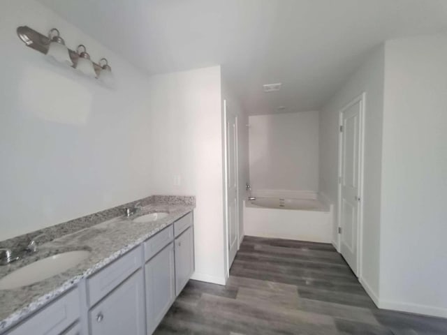 bathroom featuring wood finished floors, baseboards, a tub to relax in, and double vanity