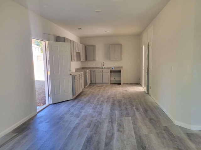 kitchen with a sink, wood finished floors, baseboards, gray cabinets, and light countertops