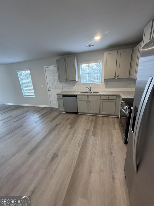 kitchen with stainless steel appliances, gray cabinets, a sink, and decorative backsplash