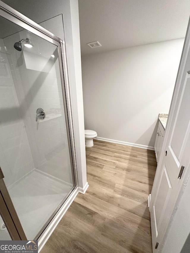 bathroom with wood finished floors, a shower stall, toilet, vanity, and baseboards