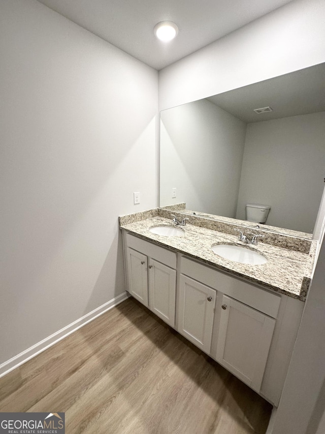 bathroom featuring wood finished floors, double vanity, toilet, and baseboards
