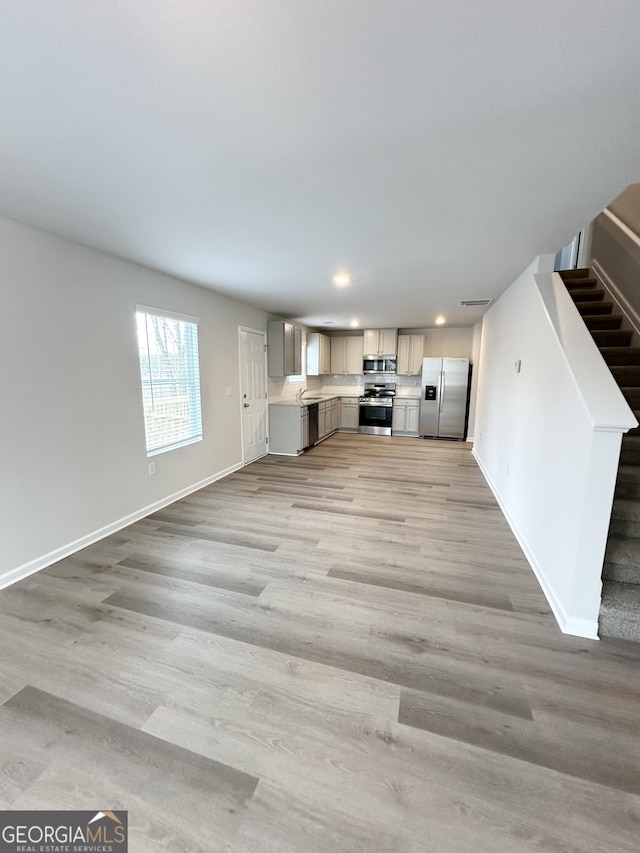 unfurnished living room with stairway, light wood-style floors, recessed lighting, and baseboards