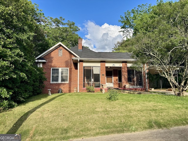 view of front of home with brick siding, a front yard, a chimney, and covered porch