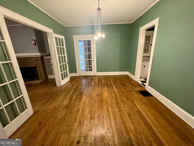 unfurnished dining area featuring wood-type flooring, baseboards, a fireplace, crown molding, and a chandelier