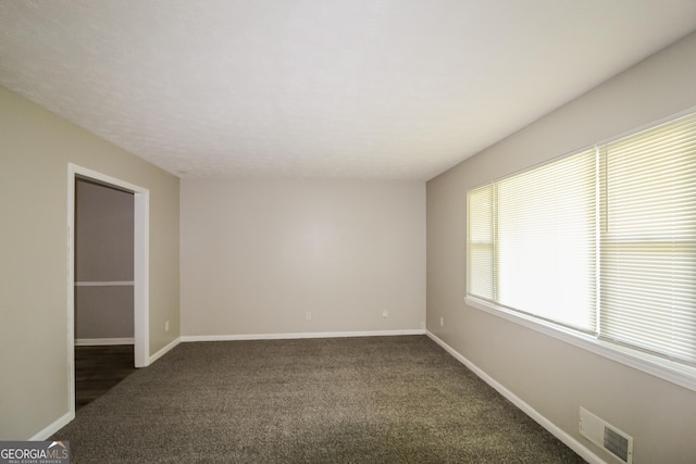 unfurnished room featuring dark carpet and baseboards