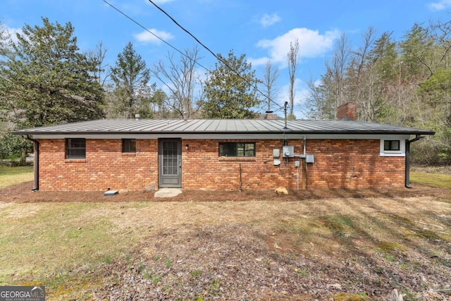 back of house featuring a chimney, brick siding, and a yard
