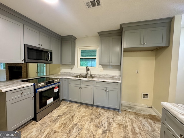 kitchen featuring stainless steel appliances, gray cabinets, a sink, and baseboards