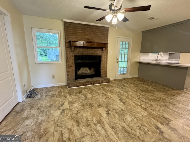 unfurnished living room featuring a textured ceiling, a ceiling fan, baseboards, a brick fireplace, and a sink