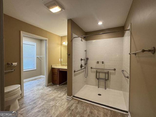 bathroom with tiled shower, vanity, baseboards, and toilet