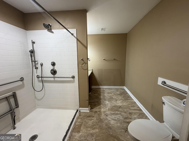 bathroom with a tile shower, toilet, baseboards, and stone finish flooring