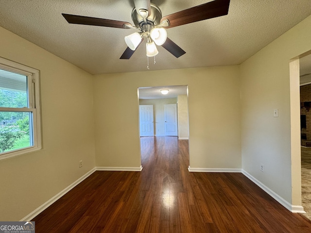 spare room with wood finished floors, ceiling fan, a brick fireplace, baseboards, and a textured ceiling