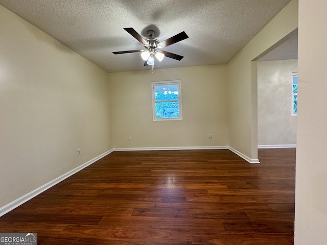 empty room with a textured ceiling, ceiling fan, dark wood finished floors, and baseboards
