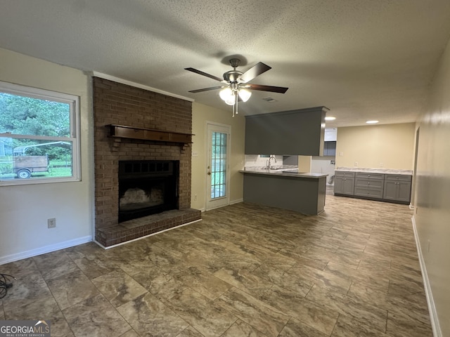 unfurnished living room with a ceiling fan, baseboards, a fireplace, a textured ceiling, and a sink