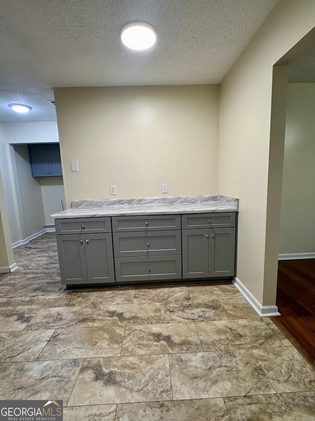 kitchen featuring gray cabinetry, a textured ceiling, baseboards, and light countertops