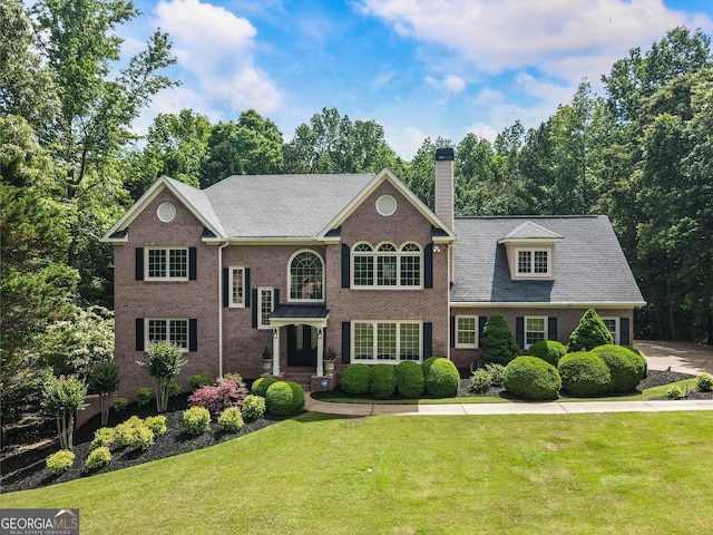 view of front of home featuring a chimney, a front lawn, brick siding, and view of wooded area
