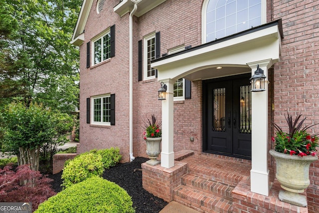 property entrance with covered porch, brick siding, and french doors